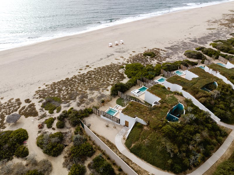 Aerial view of a luxury beachfront resort with villas and pools along the coast.