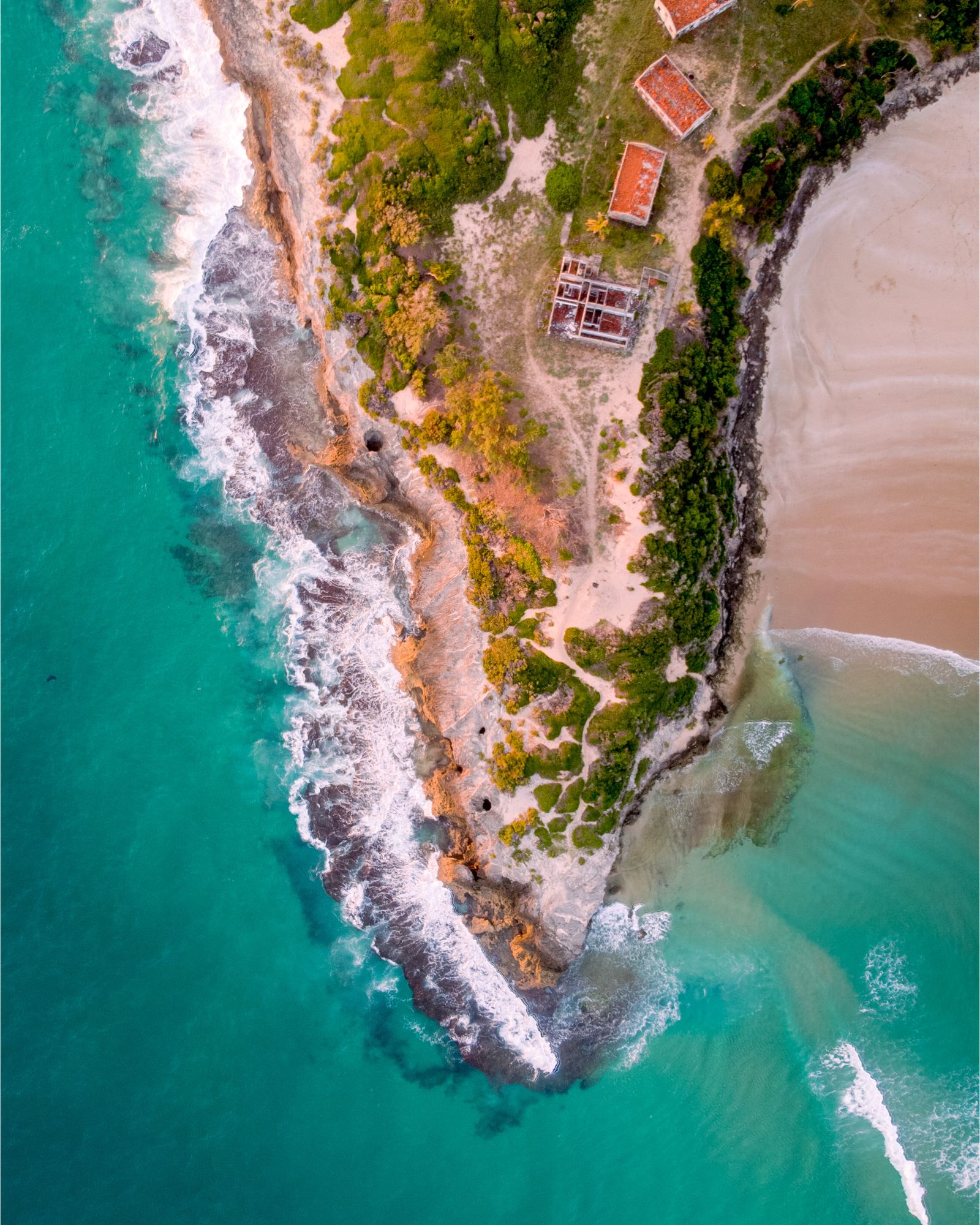Aerial view of overwater bungalows with thatched roofs connected by wooden walkways above a turquoise lagoon
